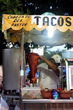 a man preparing food on top of a grill under a yellow sign that reads tacos