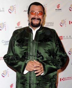 a man in a green jacket and white shirt posing for the camera with his hands on his hips
