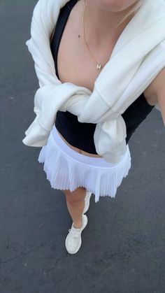 a woman wearing a white skirt and black tank top is standing in the street with her hands on her hips