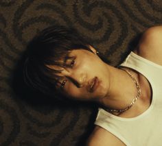 a young man laying on the floor wearing a white tank top and gold chain necklace