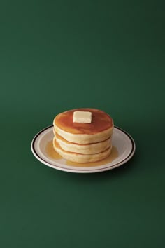 a stack of pancakes with butter on top sitting on a white plate against a green background