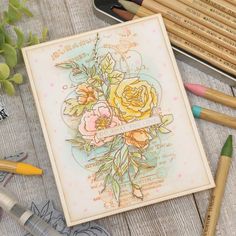 some colored pencils are laying on a table next to an art card with flowers