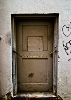 an old door is chained to the side of a white building with graffiti on it