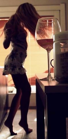 a woman standing next to a counter with a glass of wine on top of it