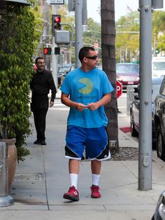 a man in blue shirt and shorts walking on sidewalk next to street with traffic lights