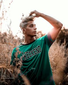 a young man standing in tall grass with his hand on his head and looking off into the distance