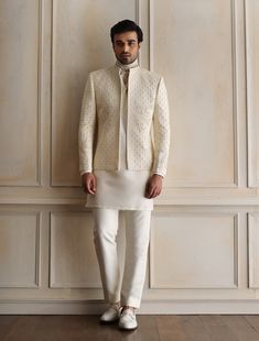 a man standing in front of a wall wearing a white suit and tie with his hands on his hips