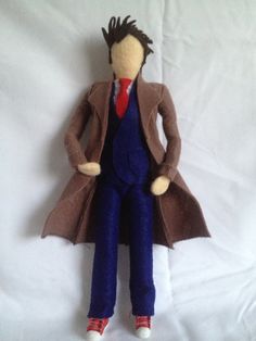 a stuffed doll is dressed in a coat and red shoes on a white sheeted surface