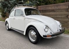a white vw bug parked in front of a wooden fence