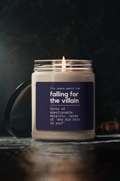 a candle sitting on top of a wooden table next to a bottle of liquid that says falling for the villain