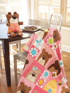 two teddy bears sitting at a table with a baby blanket on it's back