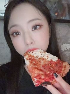 a woman eating a slice of pizza in front of her face and looking at the camera