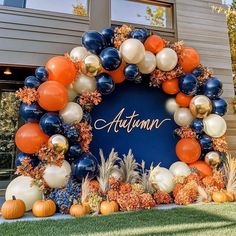an orange, white and blue balloon arch with autumn written on it in front of a building