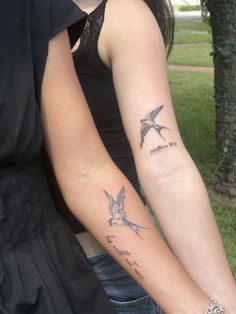 two people with matching tattoos on their arms holding each other's hands in the park