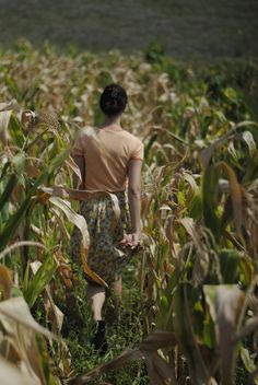 a woman walking through a field of corn