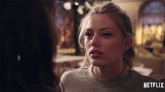 a woman talking to another person in a room with tables and lights on the walls