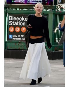 a woman walking down the street wearing a black top and white skirt with high waist