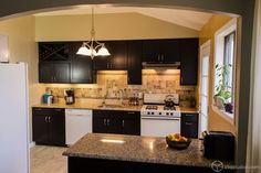 a kitchen with black cabinets, white appliances and granite counter tops is seen through an archway