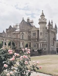 a large building with many windows and lots of flowers in the foreground on a cloudy day