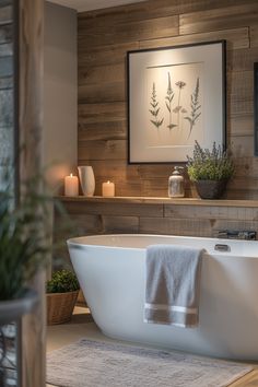 a white bath tub sitting in a bathroom next to a plant and framed art on the wall