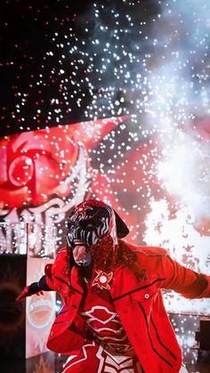 a person wearing a red jacket and black mask with fireworks in the background