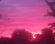 the sky is pink and purple with trees in the foreground at sunset or dawn