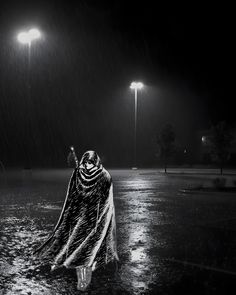 a woman walking in the rain at night with an umbrella and shawl over her head