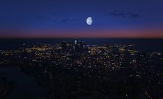 the city lights are lit up at night as the moon is seen in the distance