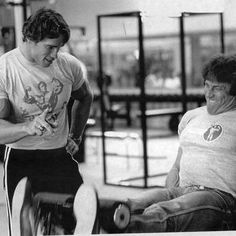 two men in a gym doing exercises with dumbbells and one man is smiling