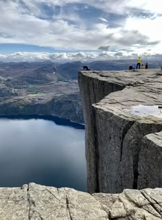 two people standing on the edge of a cliff overlooking a large body of water and mountains