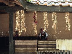a man sitting on a bench in front of a wall covered with hanging beads and cloths