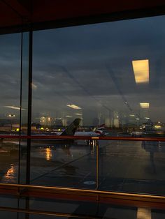 an airport terminal with planes parked on the tarmac at night, as seen through large windows