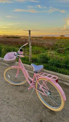 a pink bike parked on the side of a road next to a fence and grassy field