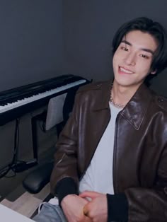 a young man sitting in front of a keyboard smiling at the camera while wearing a brown leather jacket