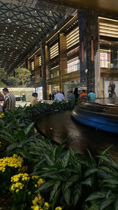 people are walking around in the lobby of an office building with water fountain and yellow flowers