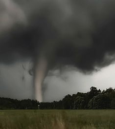 a large black cloud is in the sky over a field