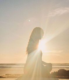 a woman sitting on top of a surfboard in front of the ocean at sunset