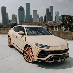 a beige sports car parked in front of a cityscape with orange rims