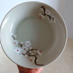 a hand holding a white bowl with flowers painted on it