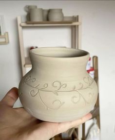 a hand holding a white vase with designs on it