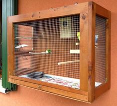 a wooden bird cage hanging on the side of a building next to a green window