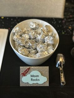 a bowl filled with silver foil sitting on top of a table next to spoons