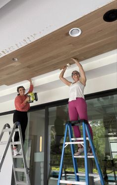 two women on ladders painting the ceiling