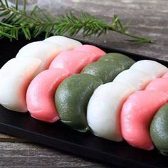 four different types of sushi on a black plate with green and pink toppings