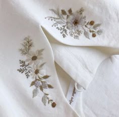two white linens with embroidered flowers on them, one is folded up and the other has
