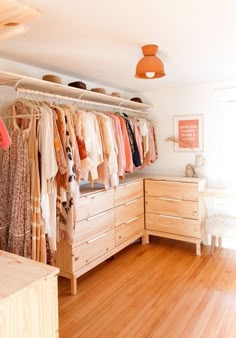 an organized closet with clothes hanging on rails and wooden drawers, in front of a window