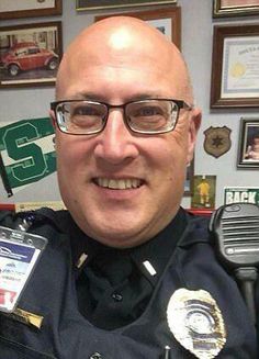 a police officer is smiling for the camera with his badge in his hand and badges on his chest