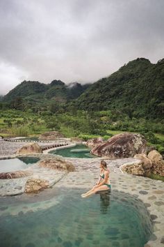 a woman sitting in the middle of a body of water with mountains in the background