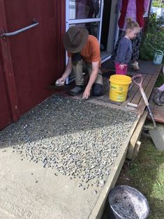 two children are playing with gravel in front of a red shed and some buckets