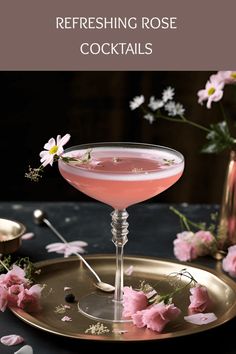 a pink cocktail in a coupe glass on a gold plate with flowers around the rim
